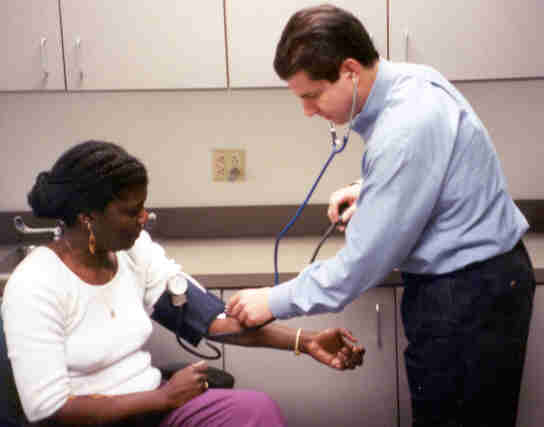 picture of the helper placing bell of the stethoscope onto bend in arm where brachial pulse can be felt